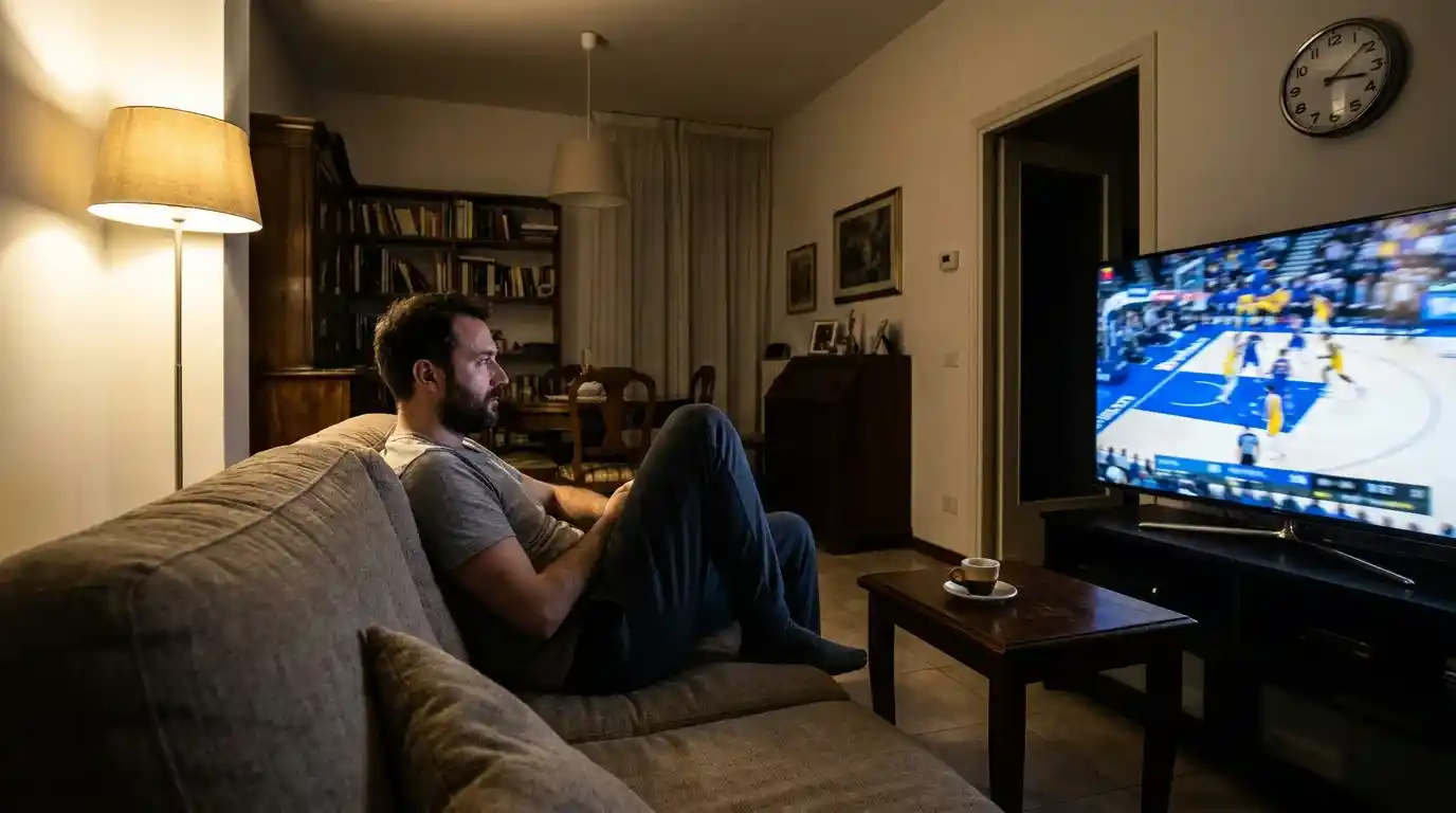 Spettatore italiano in soggiorno guarda una partita NBA notturna su grande televisore con luce soffusa