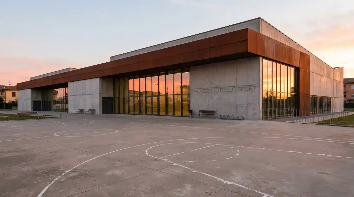 Vista esterna di un palazzetto del basket italiano al tramonto, con riflessi caldi sulle vetrate
