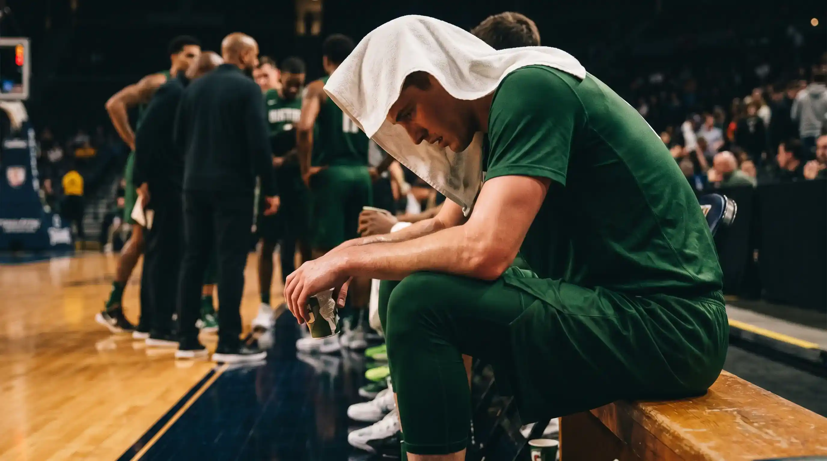 Cestista NBA seduto sulla panchina con asciugamano sulle spalle durante un timeout di partita