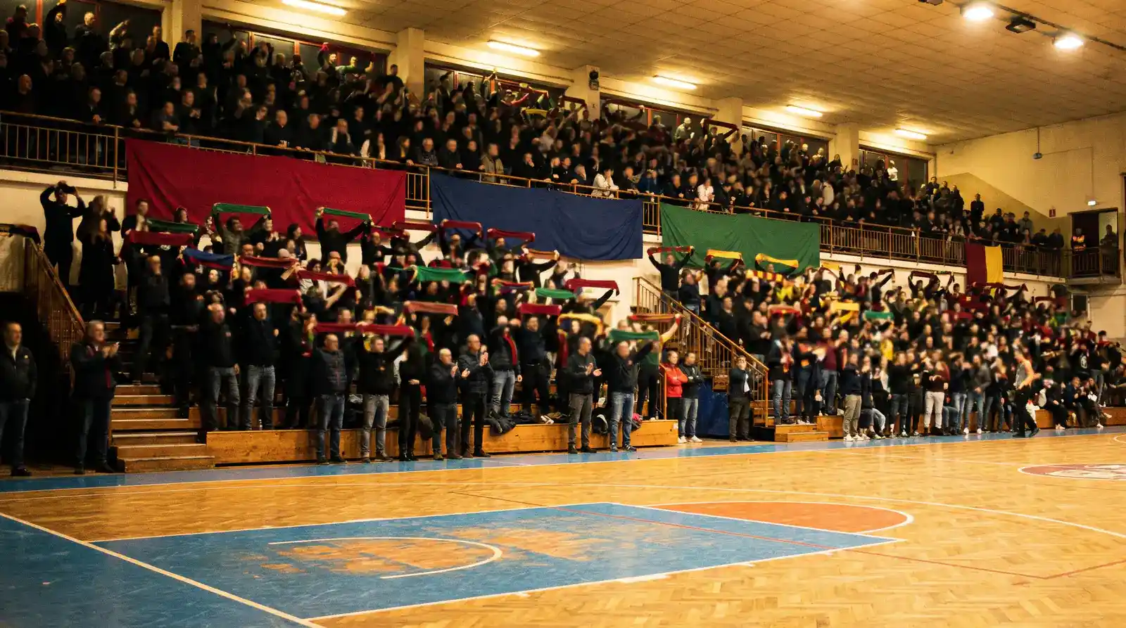Palazzetto italiano di Serie A LBA con tifoseria in piedi sugli spalti in luce calda